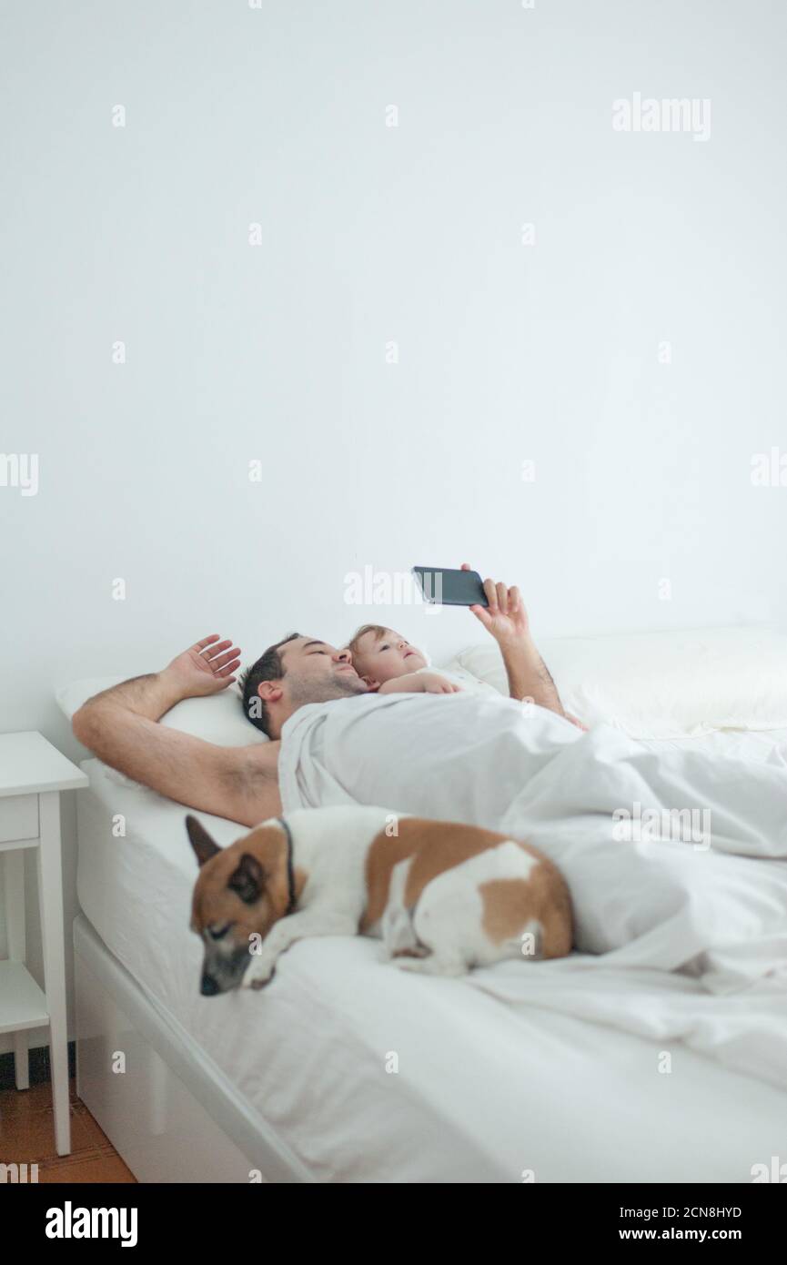 Papà e figlia che guardano lo smartphone a letto con il cane Foto Stock