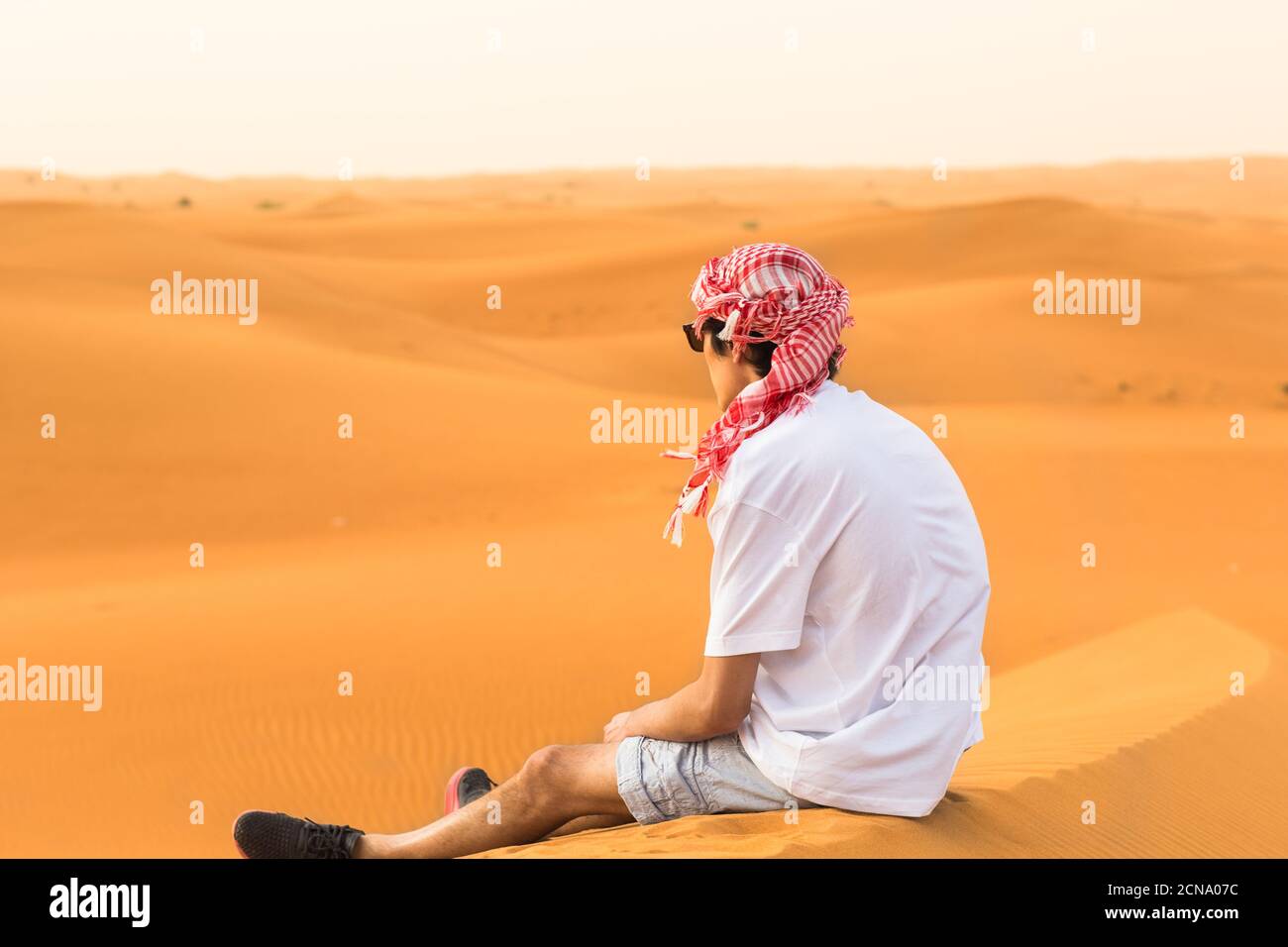 Calma giovane turista maschile seduto da solo nella duna di sabbia del deserto arabo durante un safari viaggio. Viaggi e turismo. Foto Stock