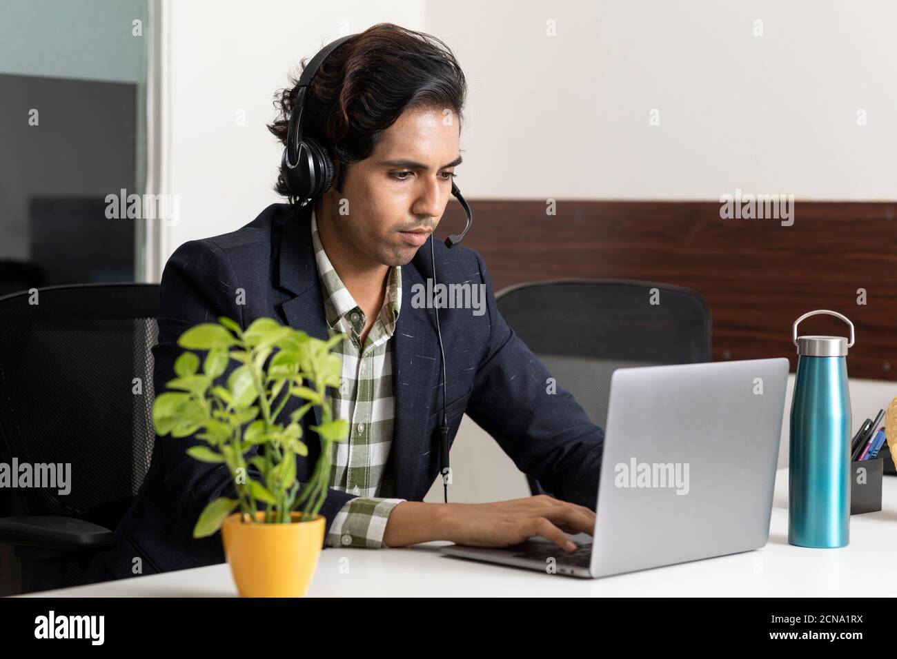Ritratto di un giovane uomo d'affari indiano che lavora dal suo laptop nella sua cabina d'ufficio, ambiente aziendale, dipendente del call center, videoconferenza. Foto Stock
