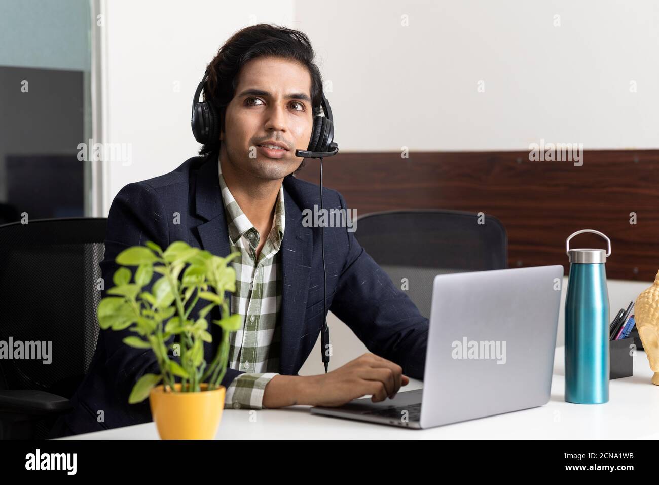 Ritratto di un giovane uomo d'affari indiano che lavora dal suo laptop nella sua cabina d'ufficio, ambiente aziendale, dipendente del call center, videoconferenza. Foto Stock