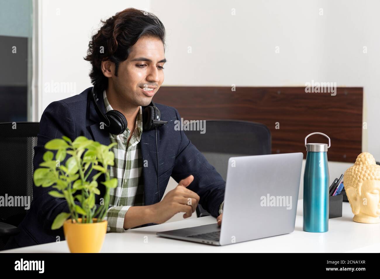 Ritratto di un giovane uomo d'affari indiano che lavora dal suo laptop nella sua cabina d'ufficio, ambiente aziendale, dipendente del call center, videoconferenza. Foto Stock