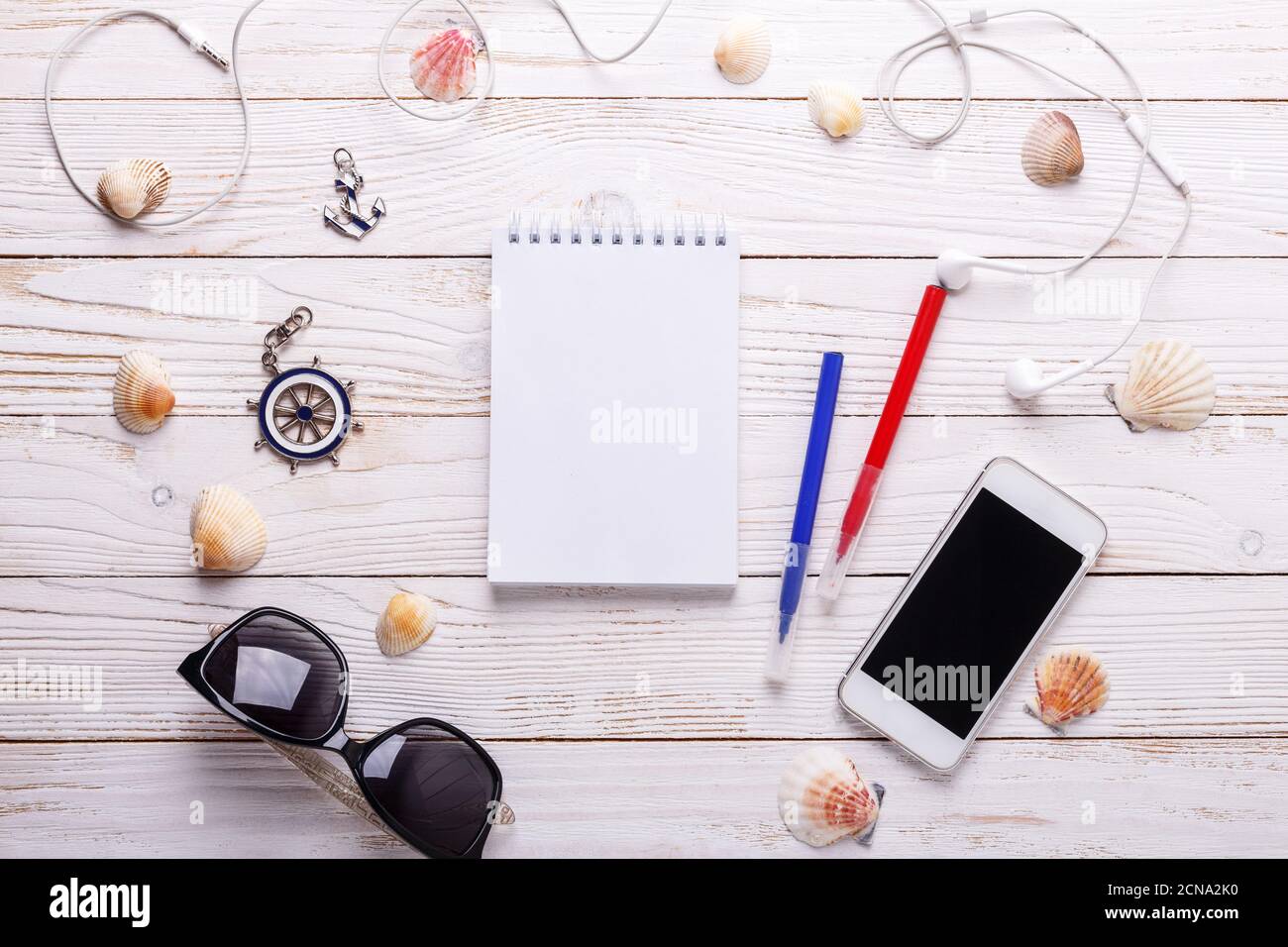 Concetto di vacanza di viaggio con cuffie, occhiali da sole, smartphone, conchiglie, notebook e t-shirt a righe. Vista dall'alto con spazio per la copia. Disposizione piatta Foto Stock