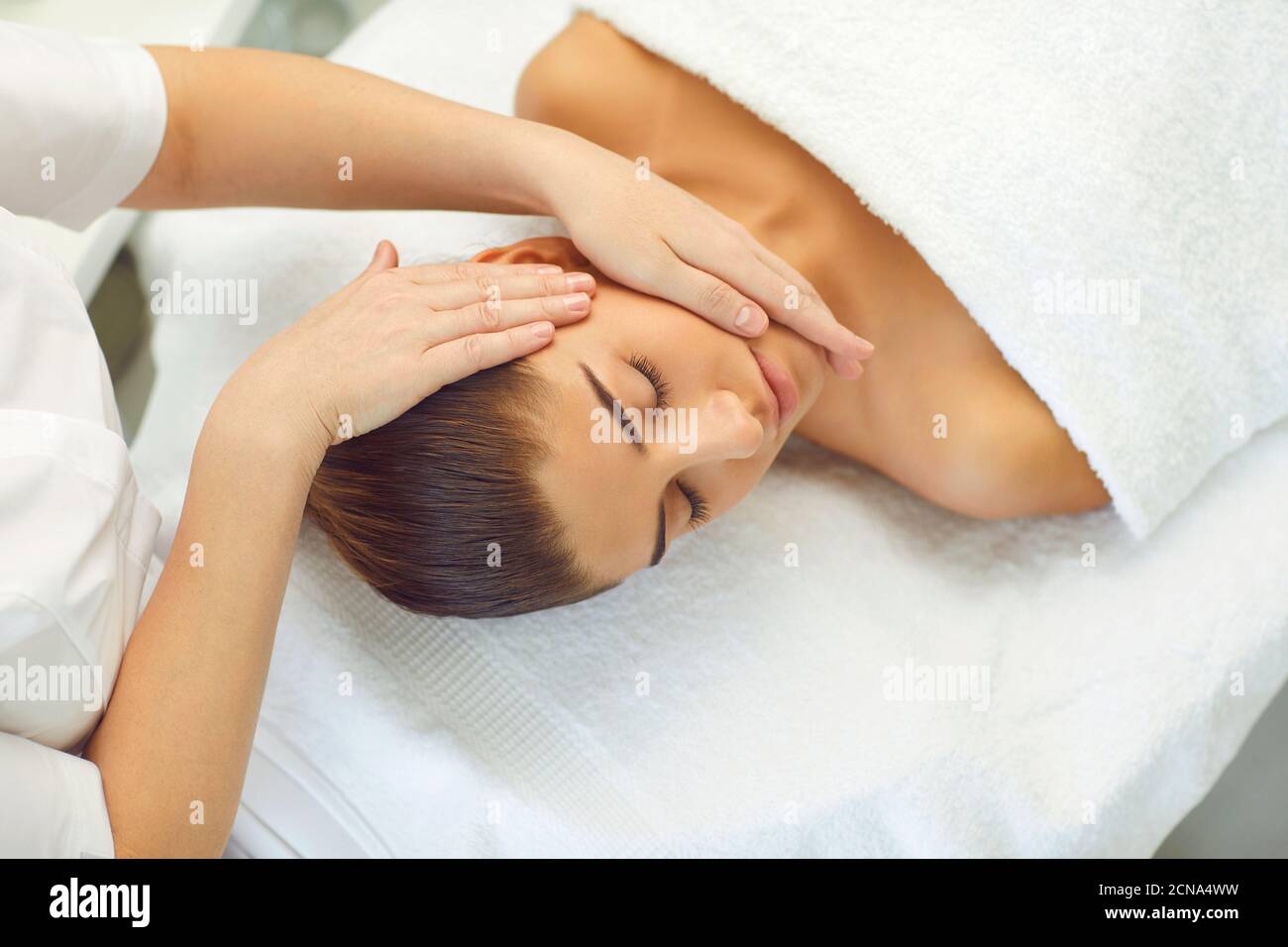 La giovane donna giace su un divano e riceve una testa massaggio dalle mani di un massaggiatore Foto Stock