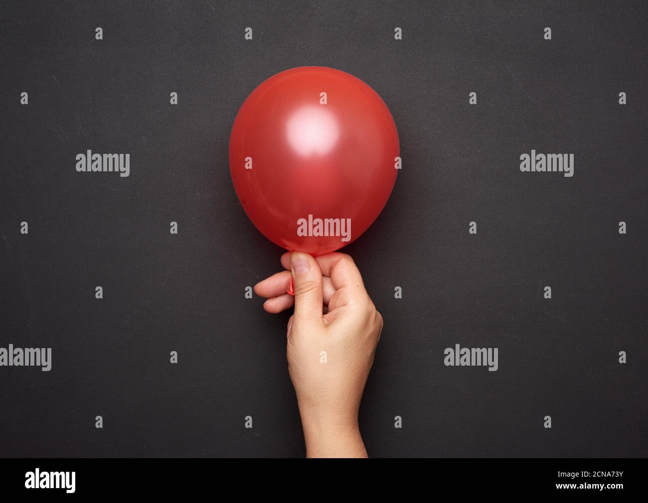 mano femmina che tiene un pallone d'aria rosso gonfiato su un sfondo nero Foto Stock