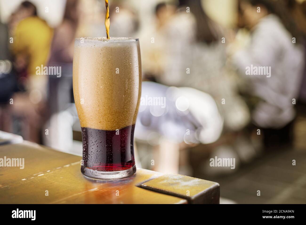 Versare la birra nera in un bicchiere al bancone di un pub. Dietro lo sfondo offuscato dei pub. Foto Stock