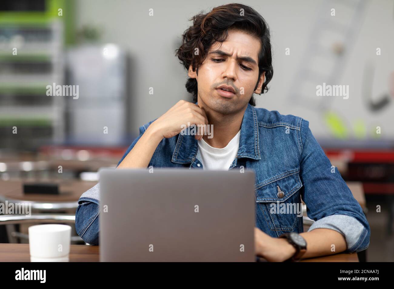 Ritratto di un giovane bell'indiano che lavora sul suo portatile, seduto in una caffetteria d'ufficio, in una caffetteria, in un ambiente di lavoro informale. Foto Stock