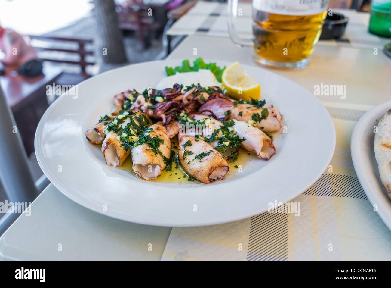 Calamari grigliati con erbe, aglio e limone su piatto bianco da vicino. Popolare e delizioso pasto mediterraneo. Foto Stock