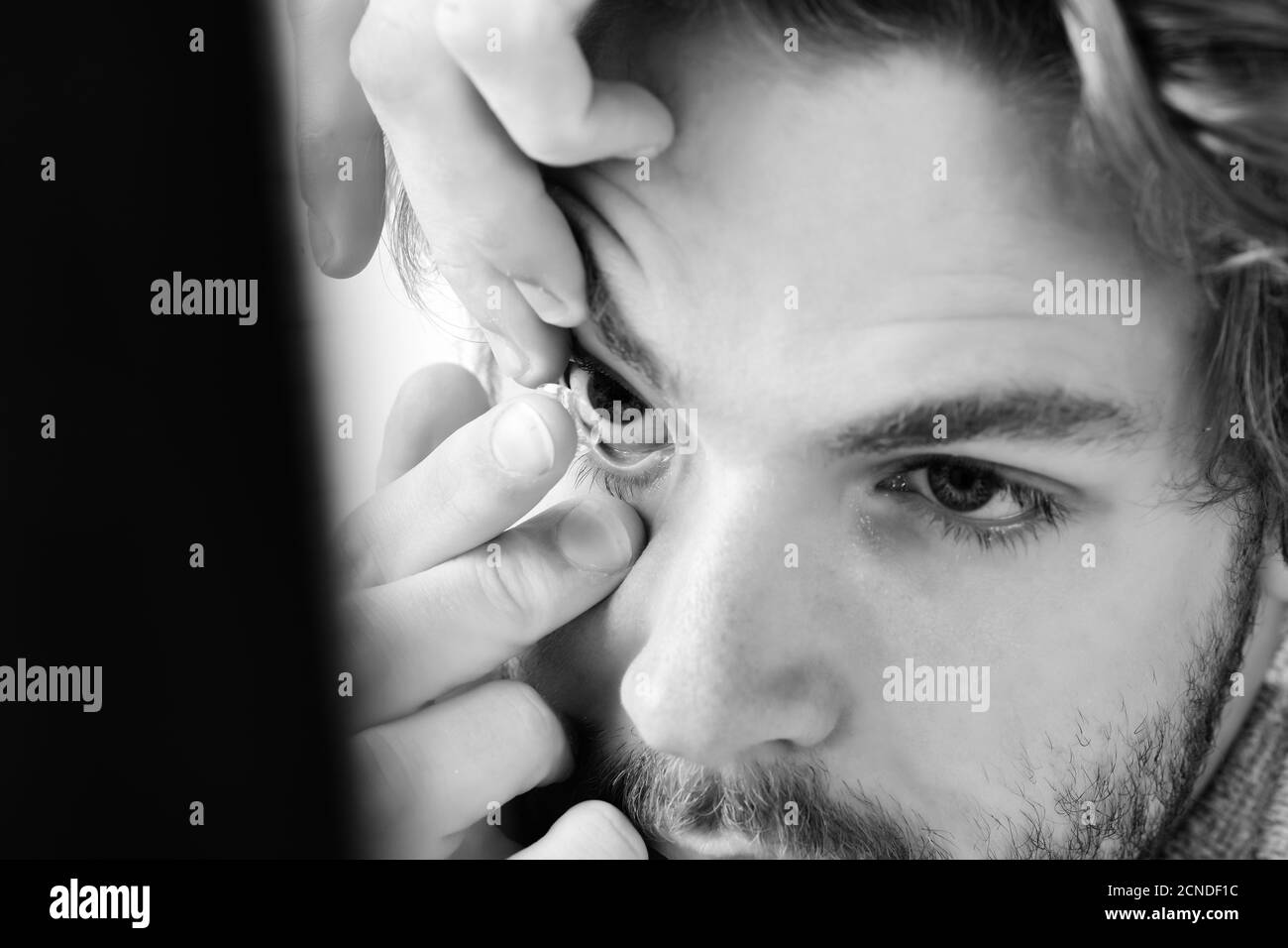 Uomo con la barba e gli occhi blu mette le lenti a contatto su, vicino. Guy detiene una lente correttiva sul suo dito, il fuoco selettivo. Salute, oftalmologia e concetto di visione Foto Stock