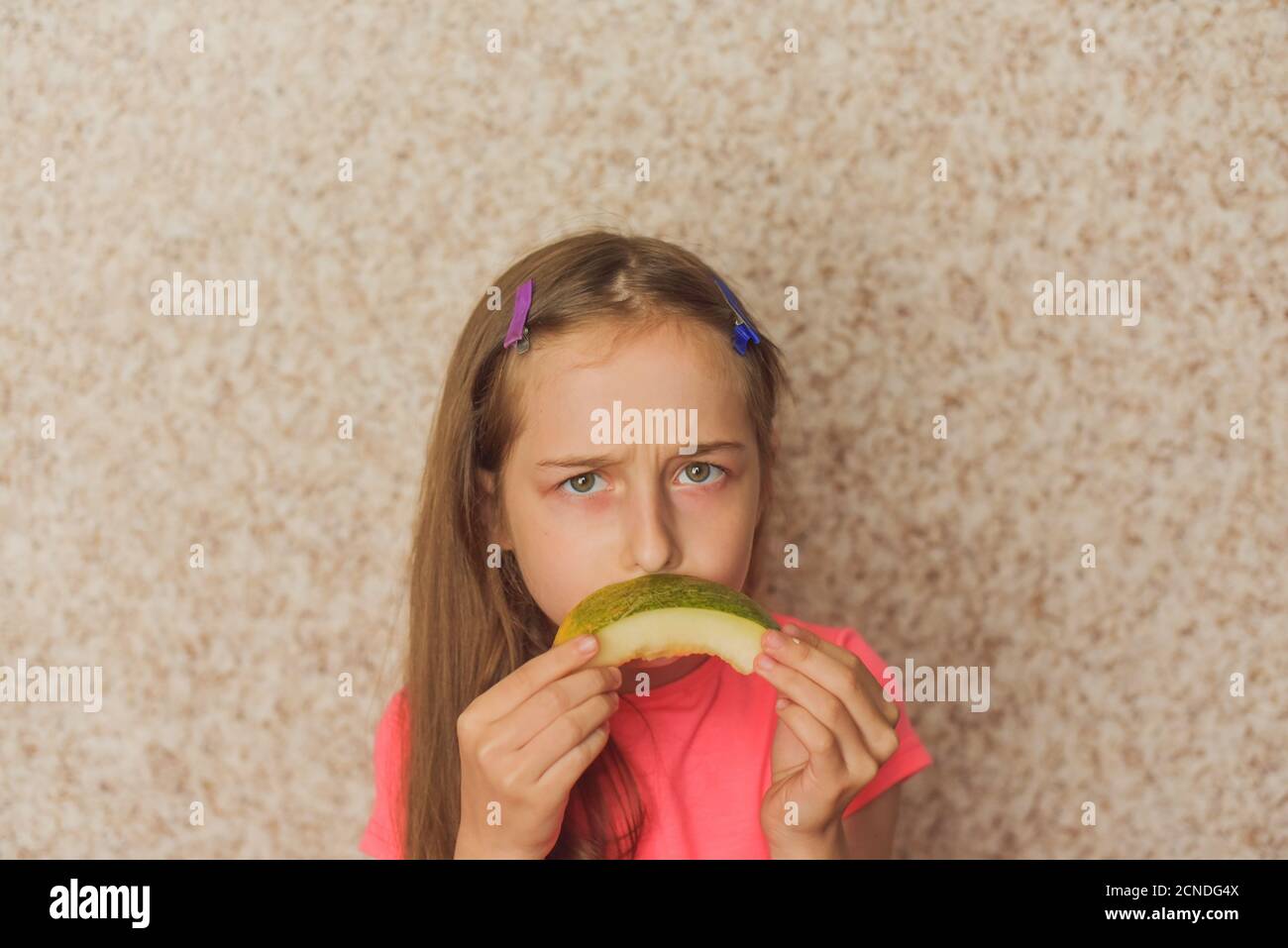 Ritratto di ragazza che mordicchiava melone. Ragazza che mangia melone. Adolescente in T-shirt rosa a casa Foto Stock