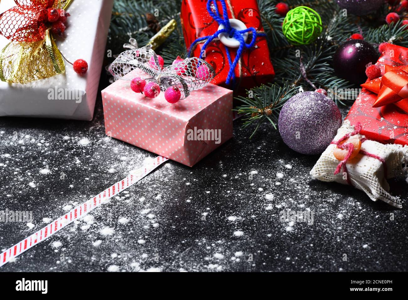 Arte di vacanza e concetto di Natale. Decorazioni natalizie su sfondo di  legno scuro con neve sparsa, copia spazio. Decorazioni realizzate in regali  rossi, rosa e bianchi. Rami di firtree con bacche