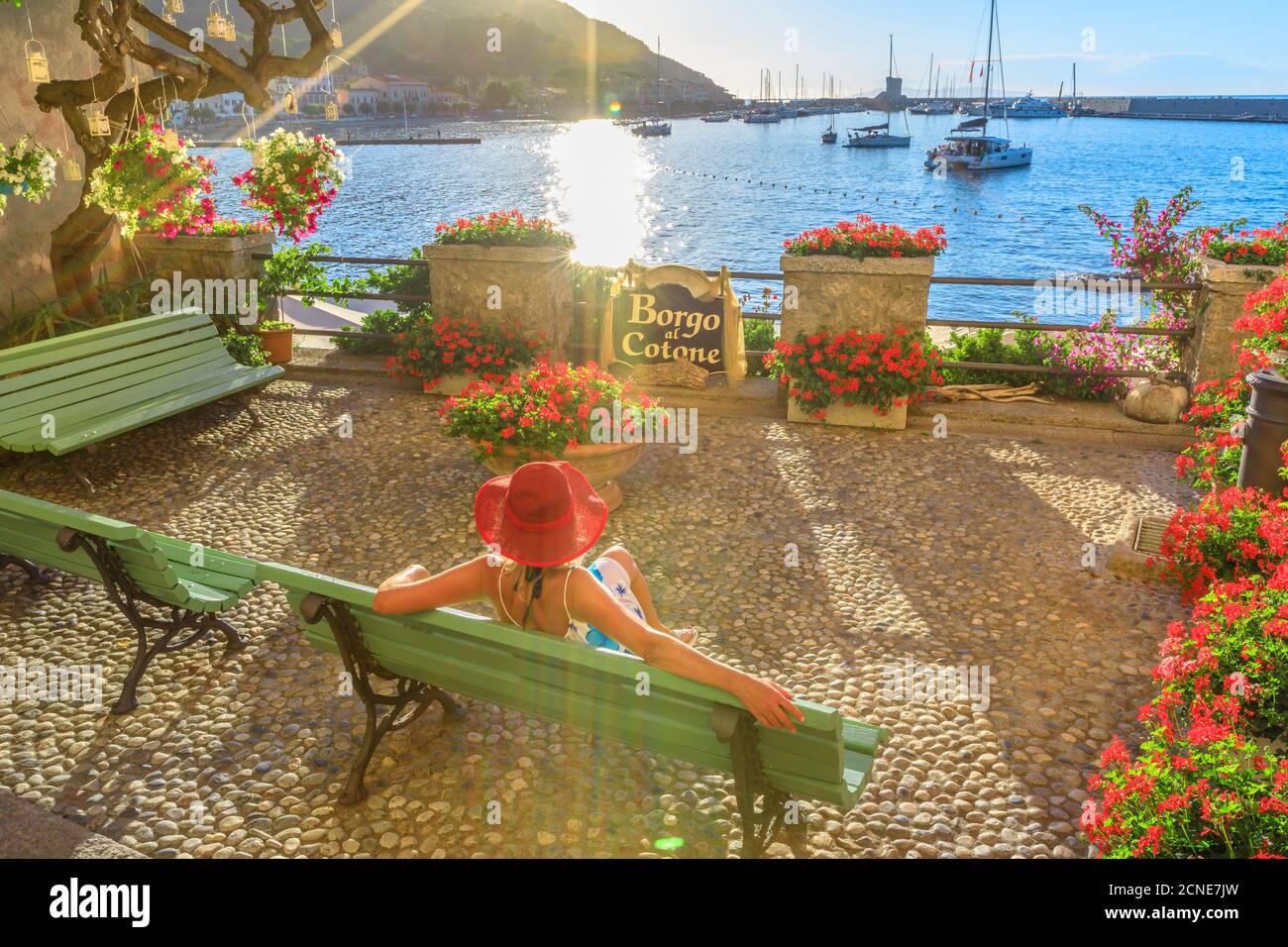 Elegante donna in rosso con cappello sul lungomare di Marciana Marina, il fiorito quartiere antico chiamato Borgo al Cotone, isola d'Elba, Arcipelago Toscano Foto Stock