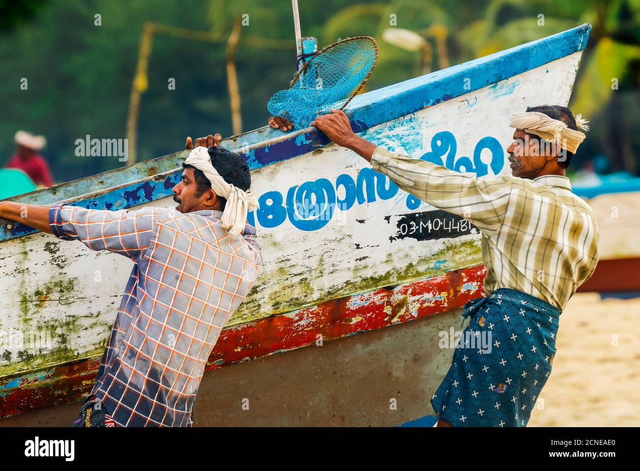 I pescatori che tirano la vecchia barca pesante sulla riva a trafficata, popolare spiaggia di Marari, Mararikulam, Alappuzha (Alleppey), Kerala, India, Asia Foto Stock