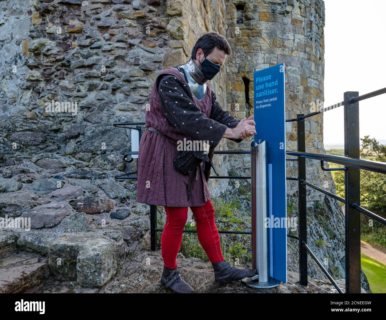 Dirleton, East Lothian, Scozia, Regno Unito, 18 settembre 2020. Riapertura del castello di Dirleton: Ambiente storico la Scozia riapre più delle sue proprietà. Oggi è il primo giorno per i visitatori del castello da quando blocco. Andrew Spratt, custode di HES, appassionato medievale e Man at Arms vestito in modo appropriato in costume medievale e indossando una maschera viso utilizza uno dei molti sanitizer mani intorno al castello Foto Stock