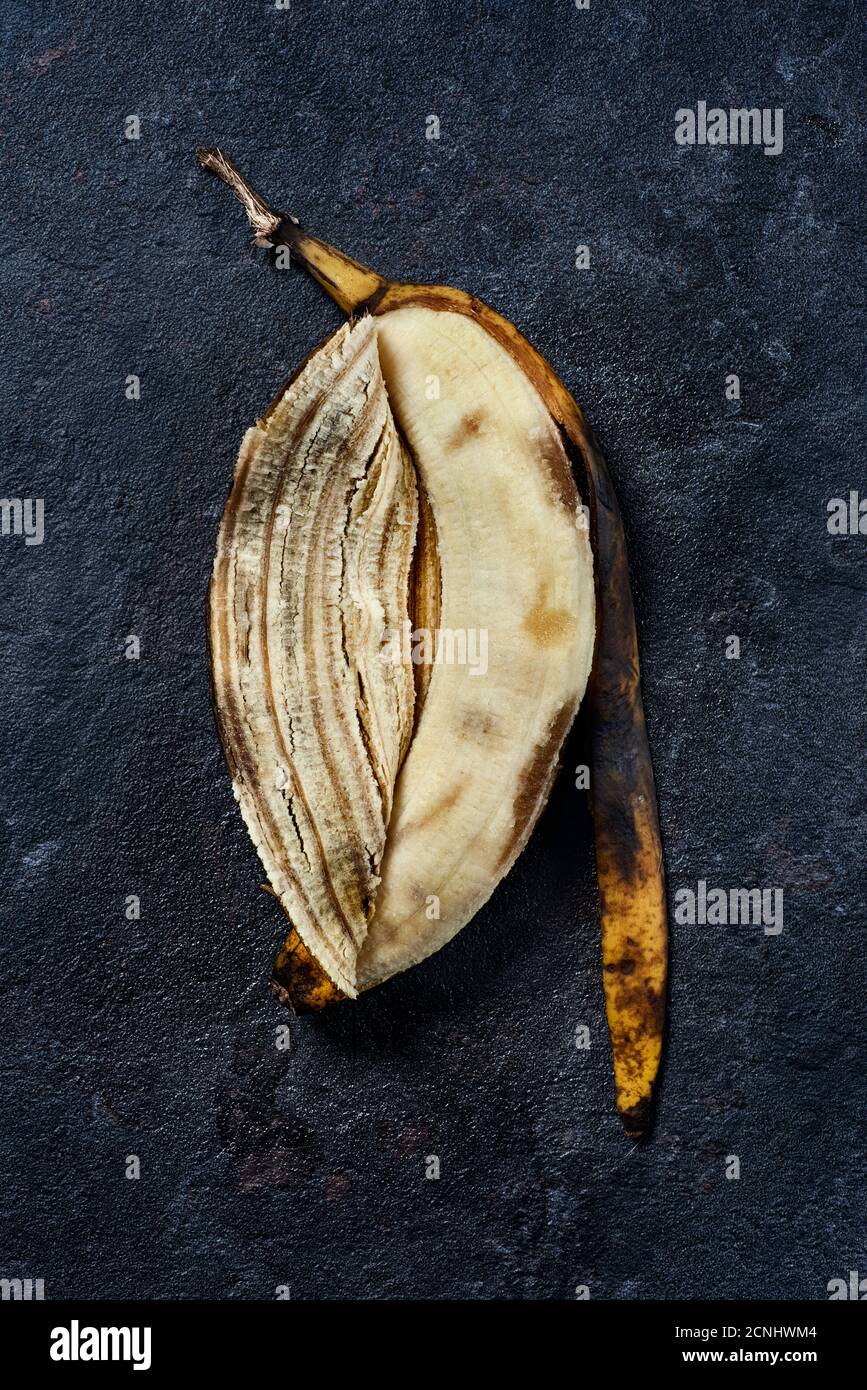 vista ad alto angolo di una banana bucciata e sopramatura pelle su una superficie di pietra nera Foto Stock