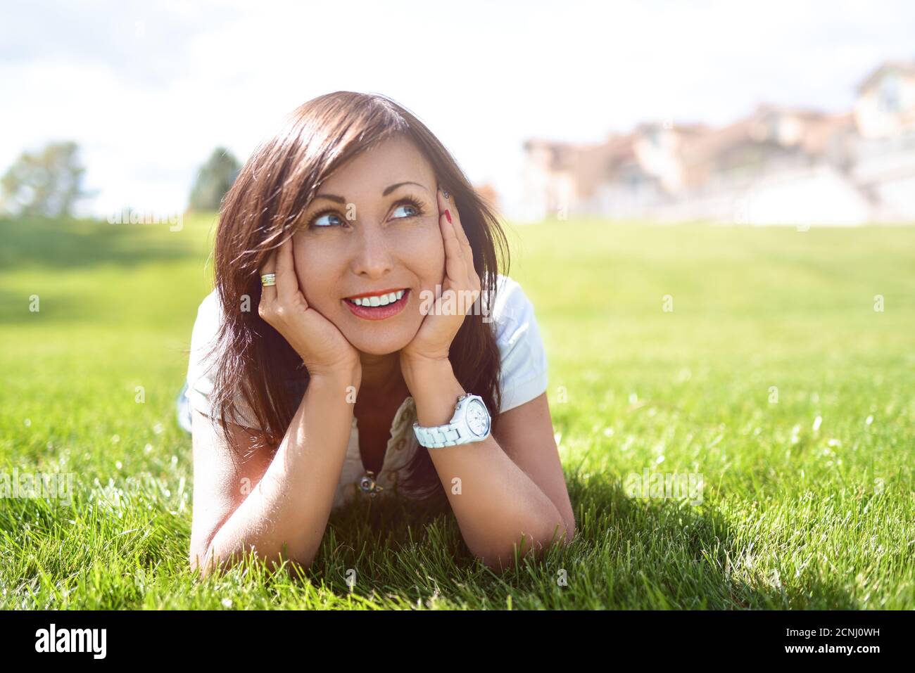 Emozione positiva, donna adulta rilassata sdraiata su erba verde in un parco all'aperto. Ragazza in occhiali da sole godendo la natura sdraiata sull'erba Foto Stock