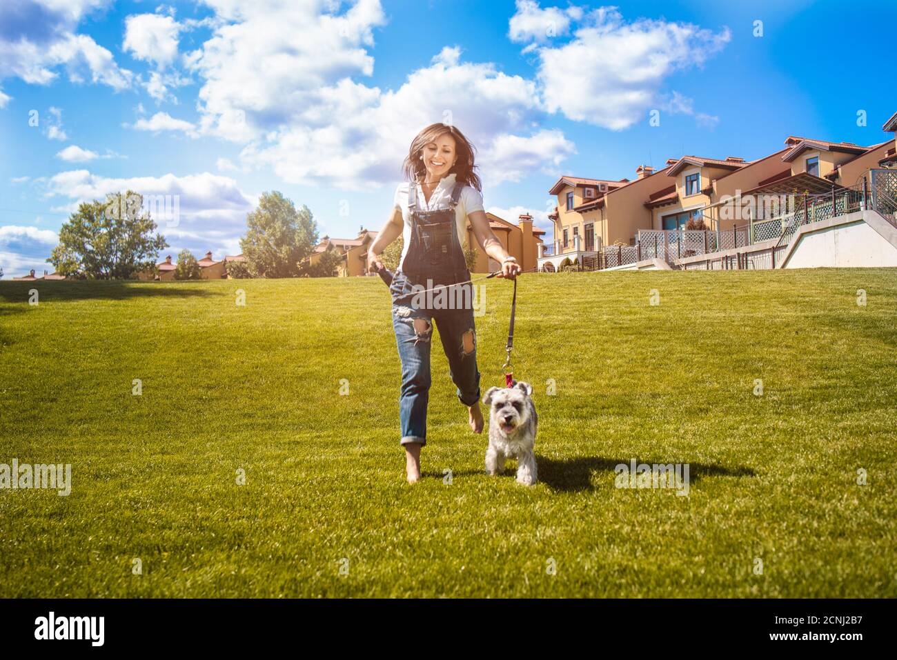 Donna caucasica adulta correre nel parco con il suo amato cane Schnauzer. Umore divertente. Concetto di amore per gli animali. Migliori amici Foto Stock