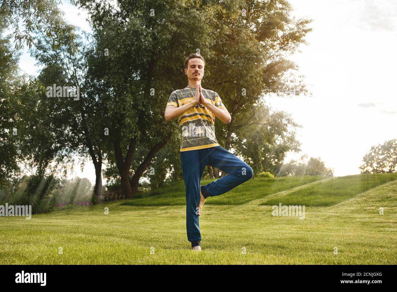 Fitness uomo che fa esercizio su una gamba isolato nel parco. Godendo natura, yoga e meditazione concetto. Spirituale pratiche.ze Foto Stock