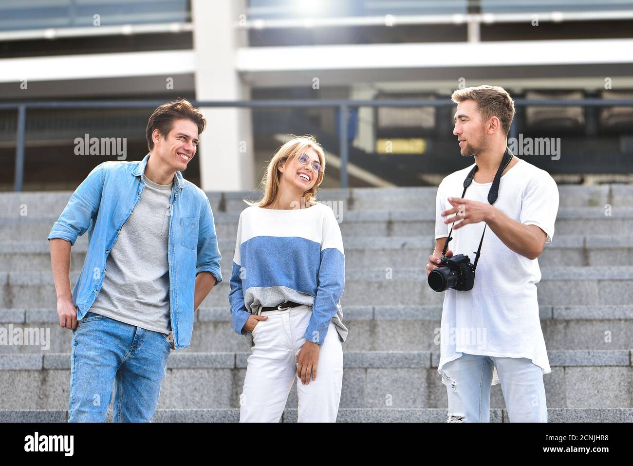 Tre amici felici che parlano una conversazione sulla strada in una giornata di sole con gli edifici sullo sfondo. Foto Stock