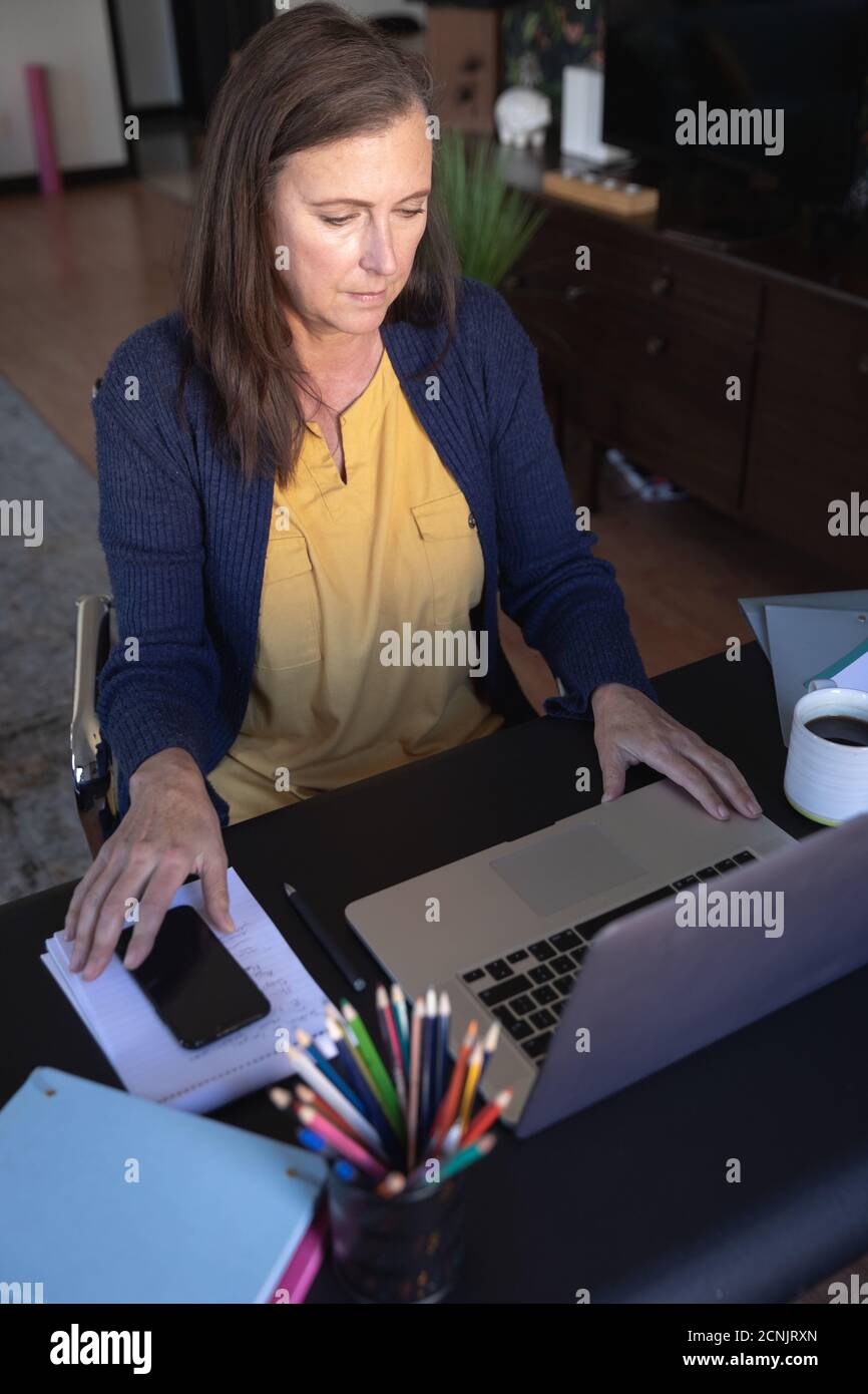 Donna caucasica godendo del tempo a casa, divaricandosi e isolandosi in quarantena, seduto al tavolo, utilizzando un computer portatile. Foto Stock