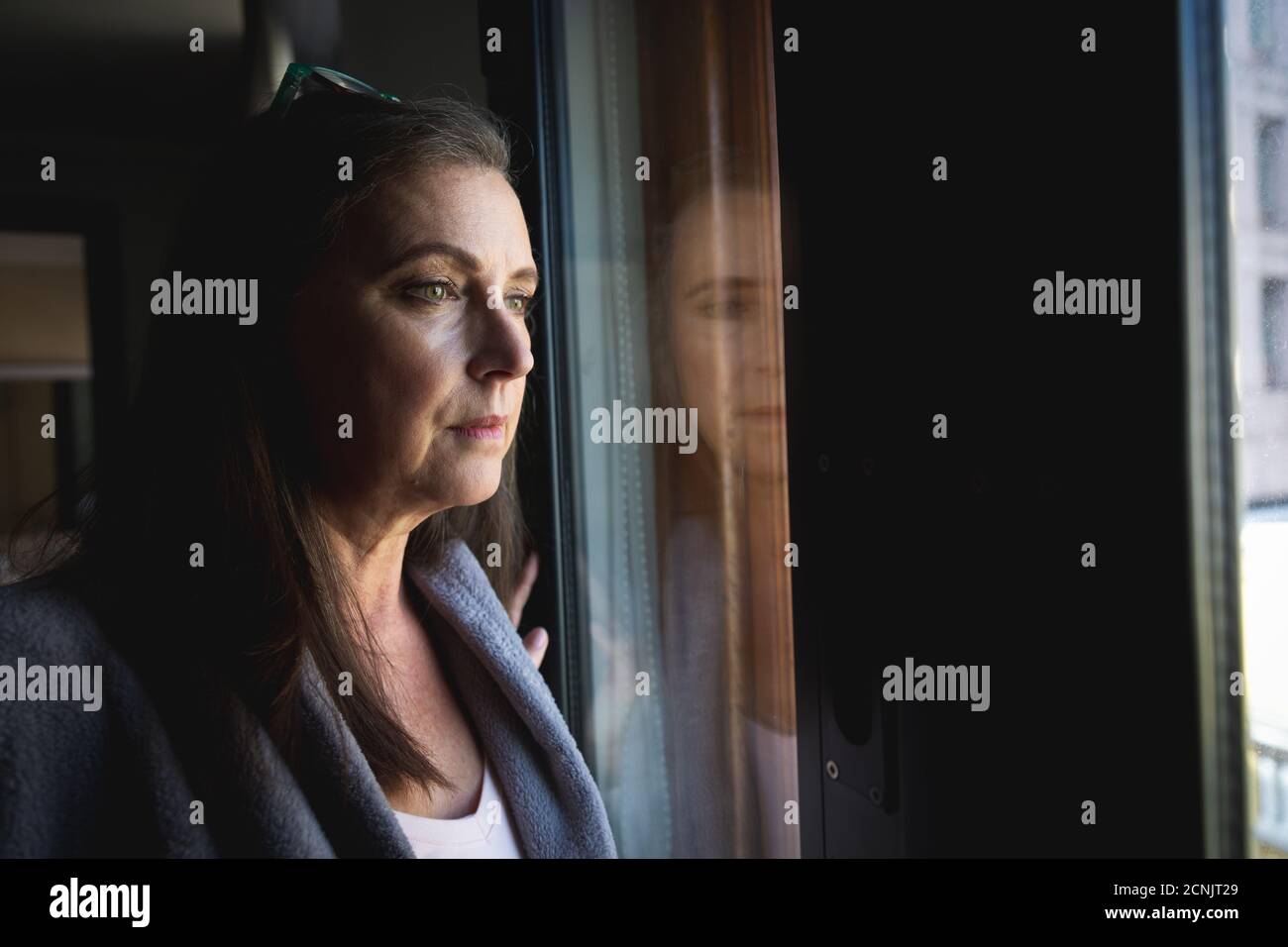 Donna caucasica con lunghi capelli scuri godendo del tempo a casa, distanziando sociale e auto isolamento in quarantena, in piedi e guardando fuori di wi Foto Stock