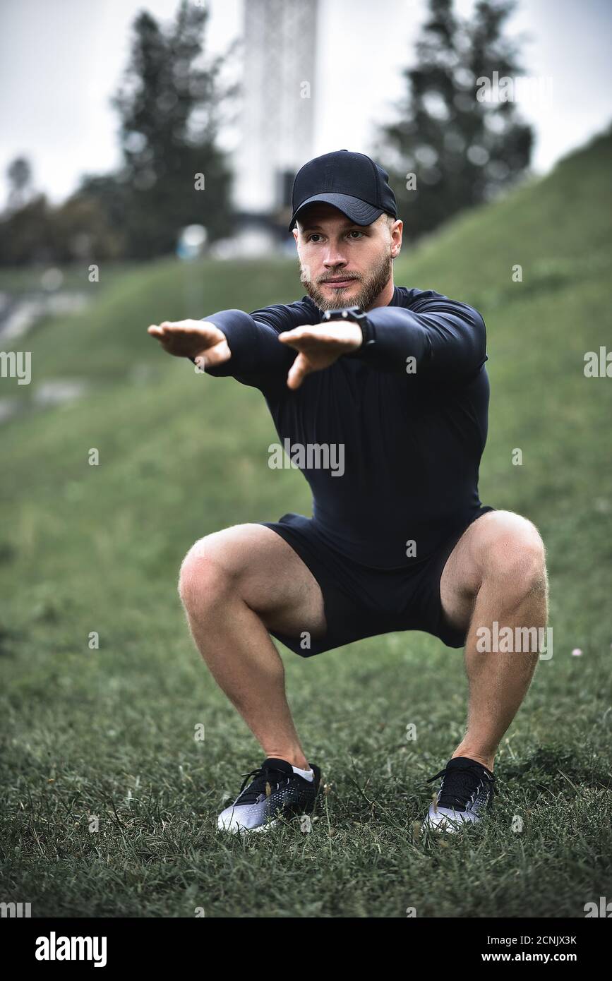 Giovane uomo attraente squatting all'aperto nel parco con le mani tese. Foto Stock