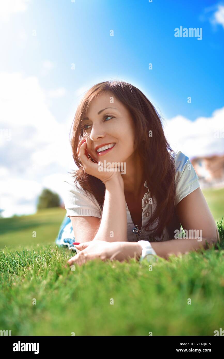 Emozione positiva, donna adulta rilassata sdraiata su erba verde in un parco all'aperto. Ragazza in occhiali da sole godendo la natura sdraiata sull'erba Foto Stock