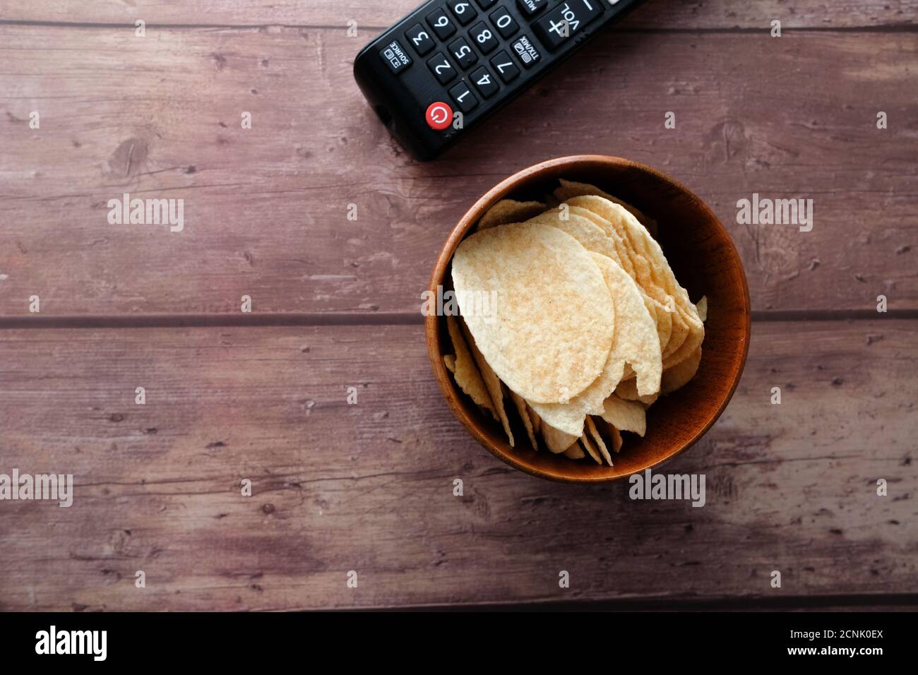 ciotola di patatine e telecomando tv su sfondo di legno. Foto Stock