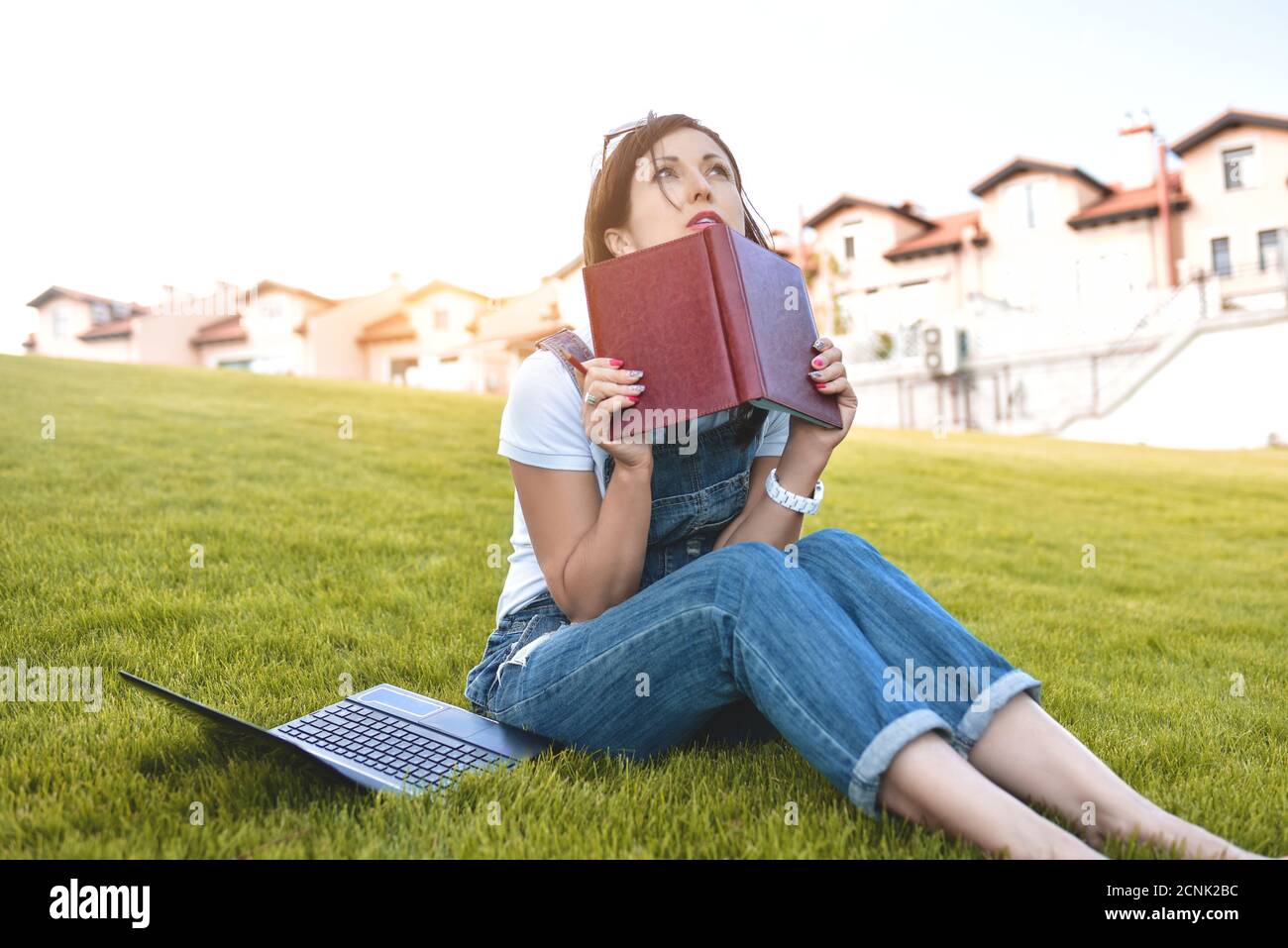 Ritratto di bella donna adulta seduta su erba verde in parco con computer portatile sulle gambe, trascorrere la giornata estiva lavorando all'aperto, utilizzando la Foto Stock