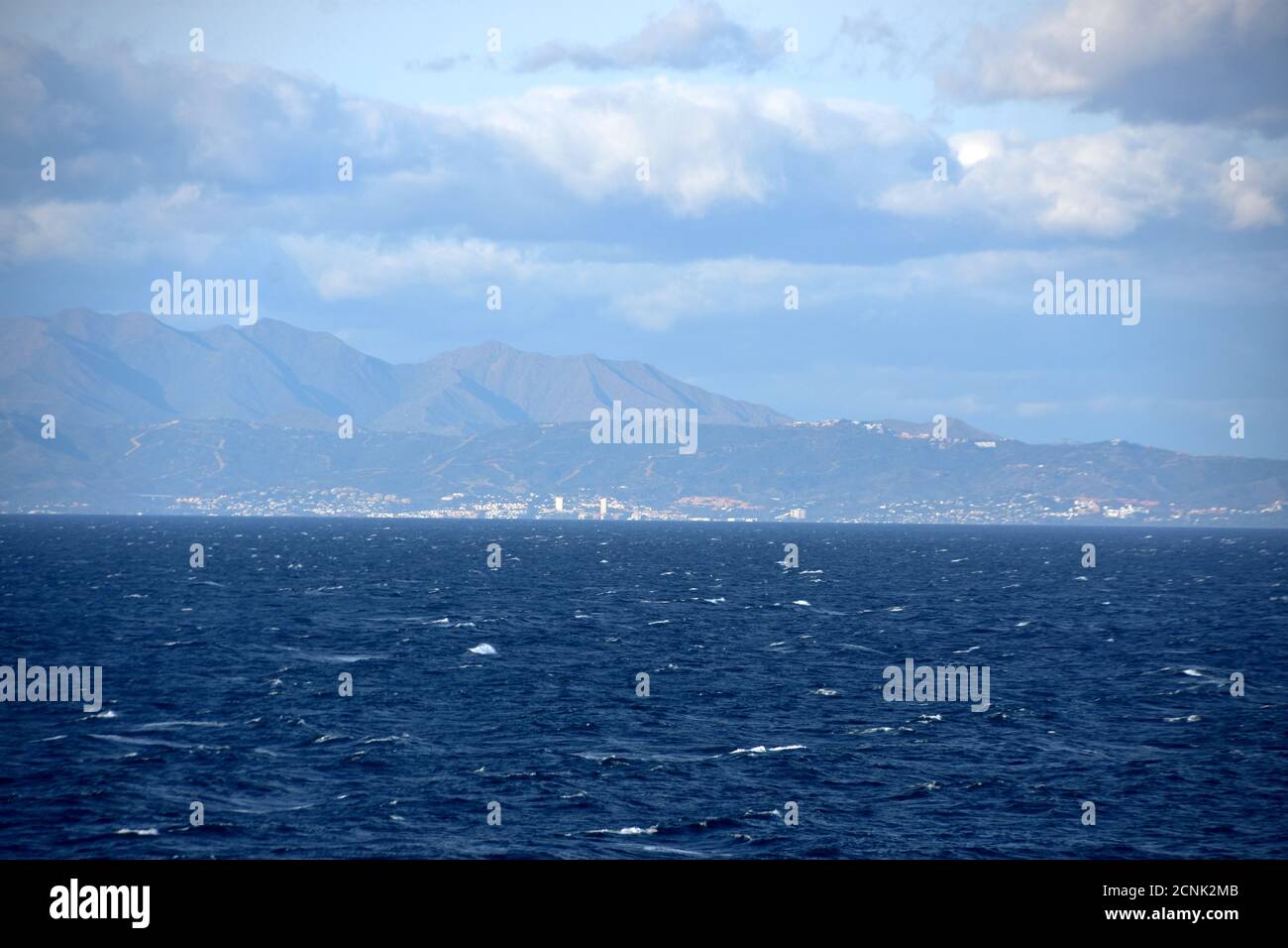 La costa mediterranea montagnosa del Marocco dietro lo stretto di Gibilterra con il paesaggio urbano durante il tempo ventoso sovrastato con il mare moderatamente ruvido. Foto Stock