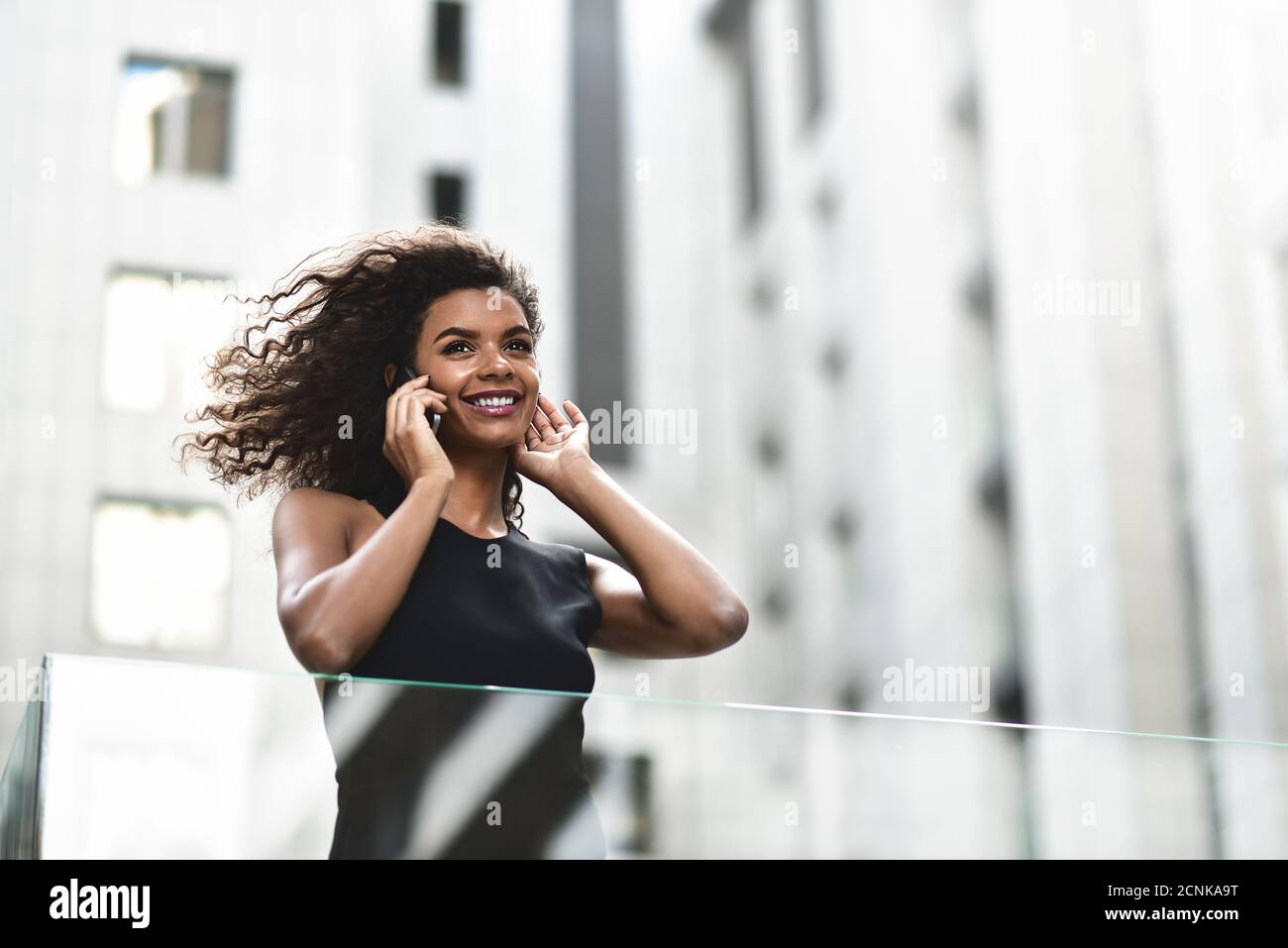 Una bella donna d'affari mista parla per telefono in città. Foto Stock