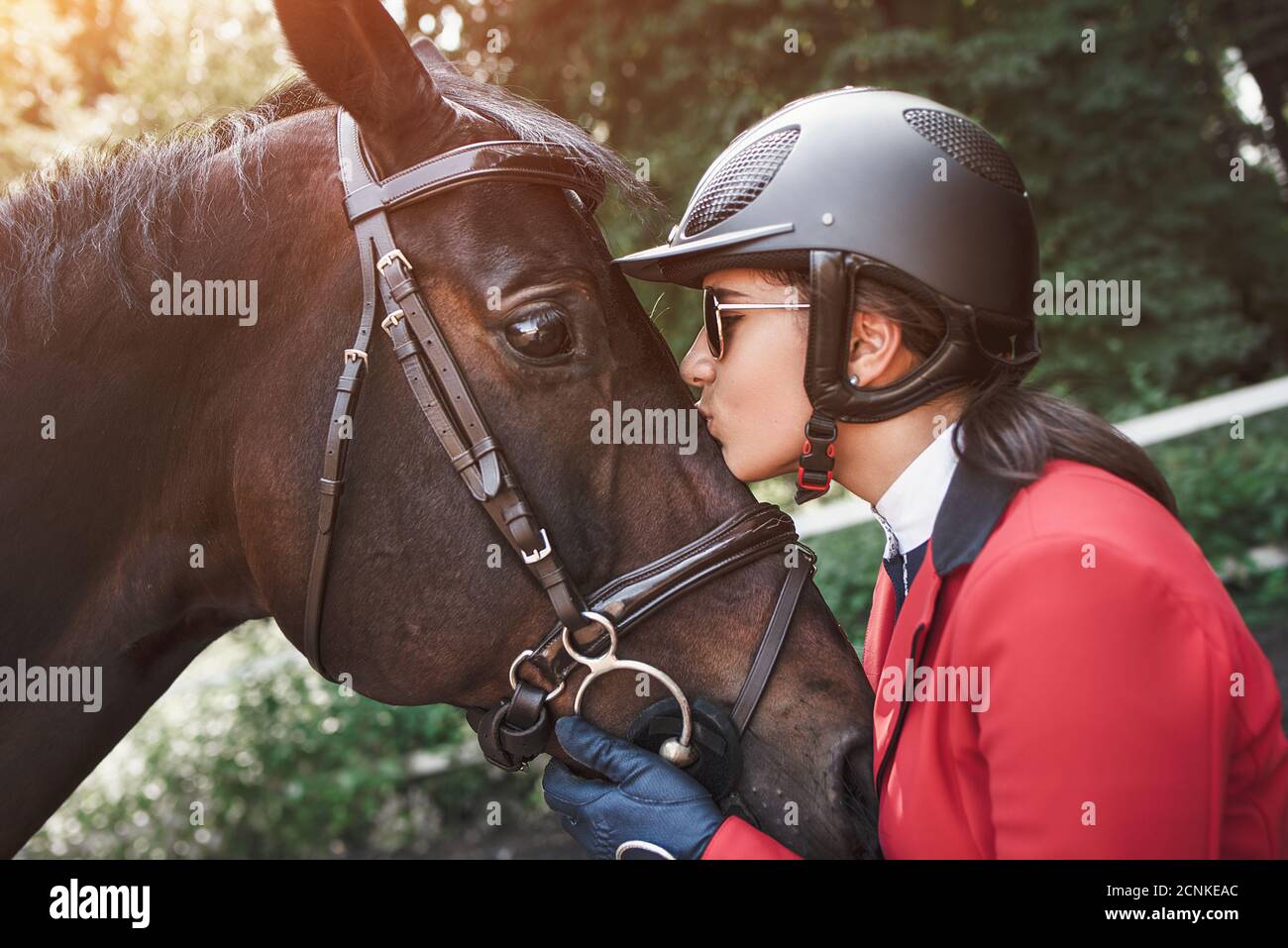 Una giovane ragazza jockey che parla e bacia il suo cavallo. Ama gli animali e con gioia trascorre il suo tempo nel loro ambiente. Foto Stock