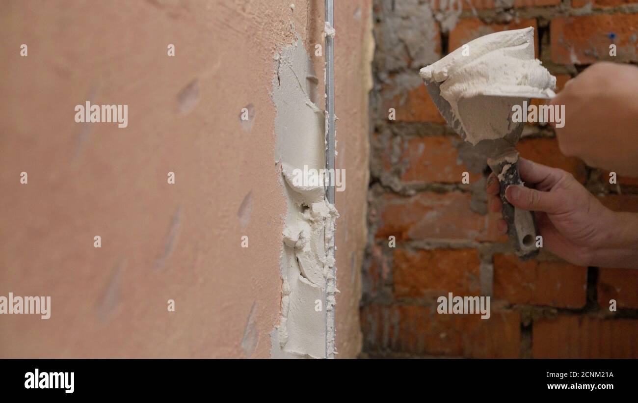 Il lavoratore mette il mastice sullo strumento. Primo piano della mano di una donna con una spatola in metallo per applicare lo stucco sulla parete Foto Stock