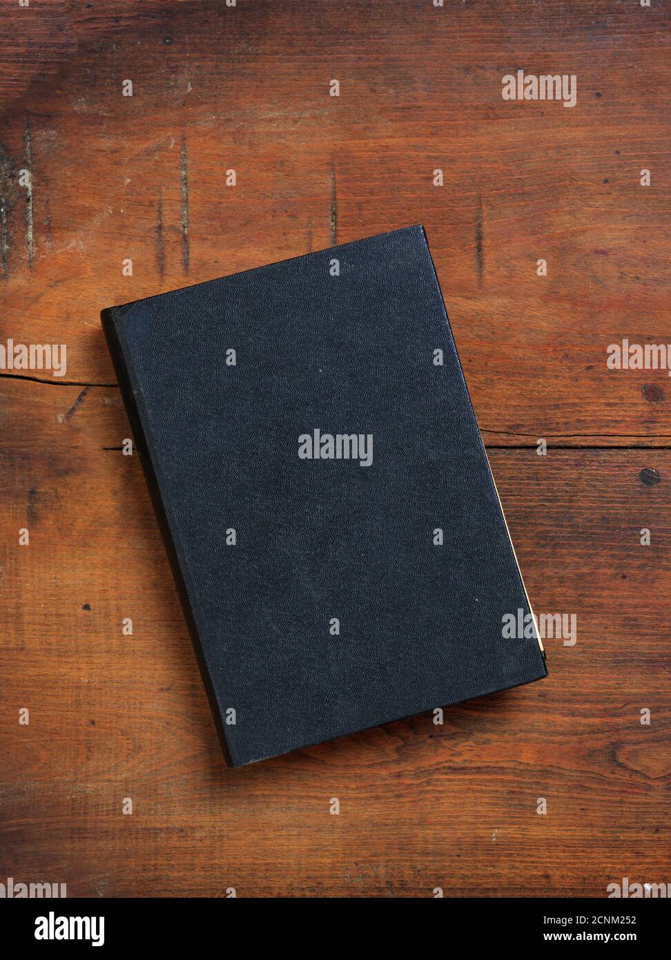 Libro nero vuoto su sfondo tavola di legno. Vecchio libro di copertina rigido chiuso d'epoca, modello di copertina, vista dall'alto, verticale Foto Stock