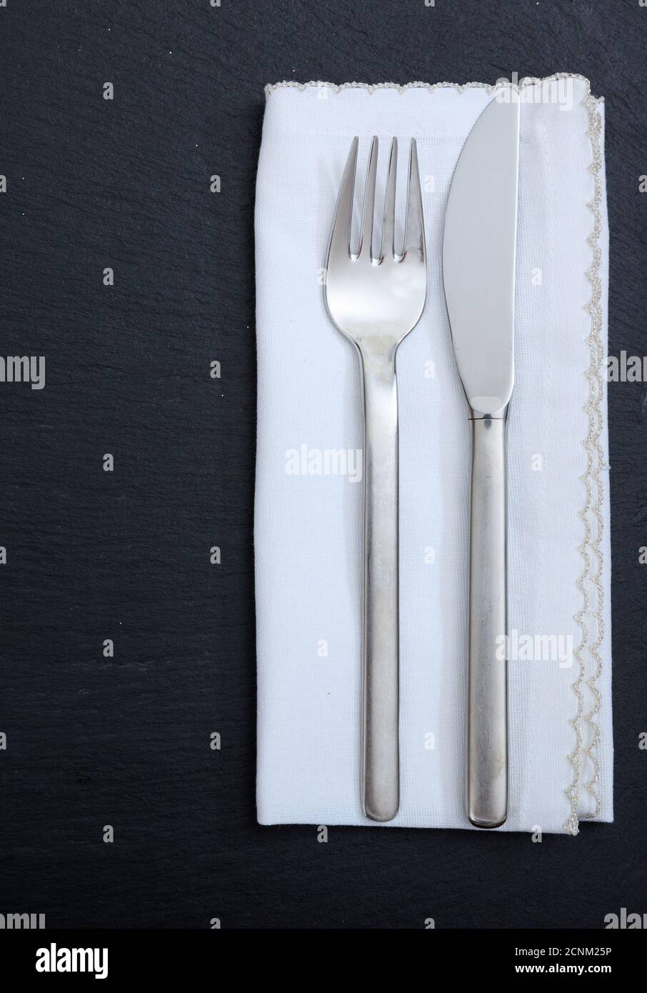 Impostazione del tavolo, pranzo di lavoro. Coltello a forchetta e tovagliolo in lino bianco isolato su sfondo nero, vista dall'alto verticale Foto Stock