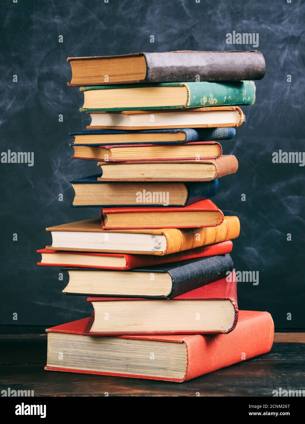 Libri accatastati su una scrivania di legno, sfondo lavagna. Vecchi libri di copertina rigida d'epoca, scuola, istruzione, concetto di scienza. Foto Stock