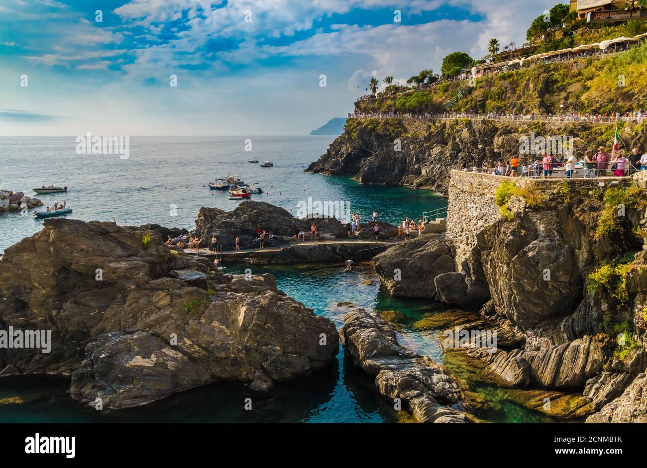Splendida vista panoramica sulla zona costiera di Manarola vicino al porto turistico in una giornata di sole con cielo blu. I turisti stanno seguendo il sentiero... Foto Stock