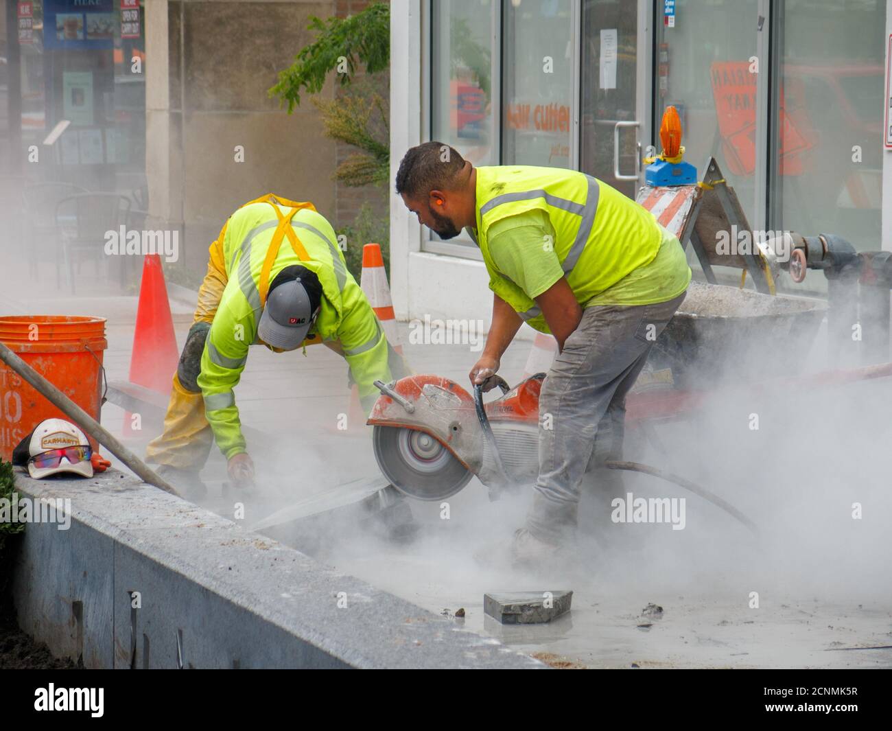 Lavoro con sega circolare raffreddata ad acqua che taglia i blocchi di pavimentazione della pietra. Progetto di ricostruzione di Lake Street. Oak Park, Illinois. Foto Stock