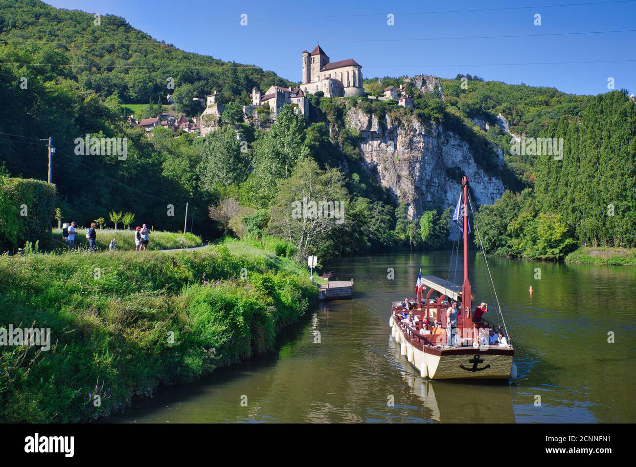 Una vista panoramica del pittoresco villaggio di St Cirq-Lapopie con il fiume, una barca passeggeri e gola in primo piano, Midi iPyrenees, Lot, Cahors, Francia Foto Stock