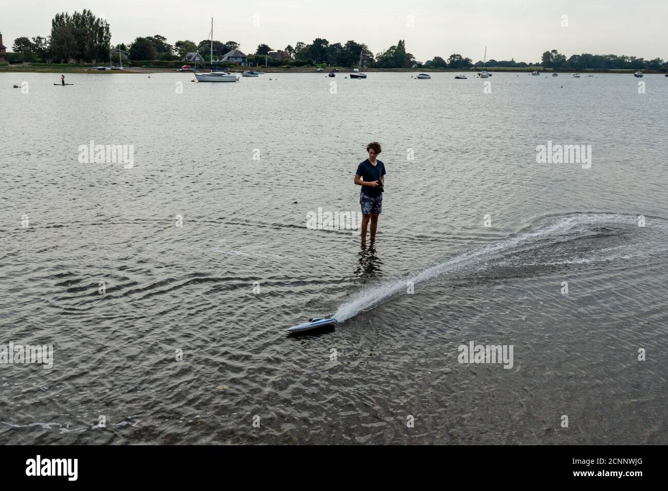 Giovane uomo in piedi in acque di mare poco profonde giocando con un modello di imbarcazione con telecomando Foto Stock