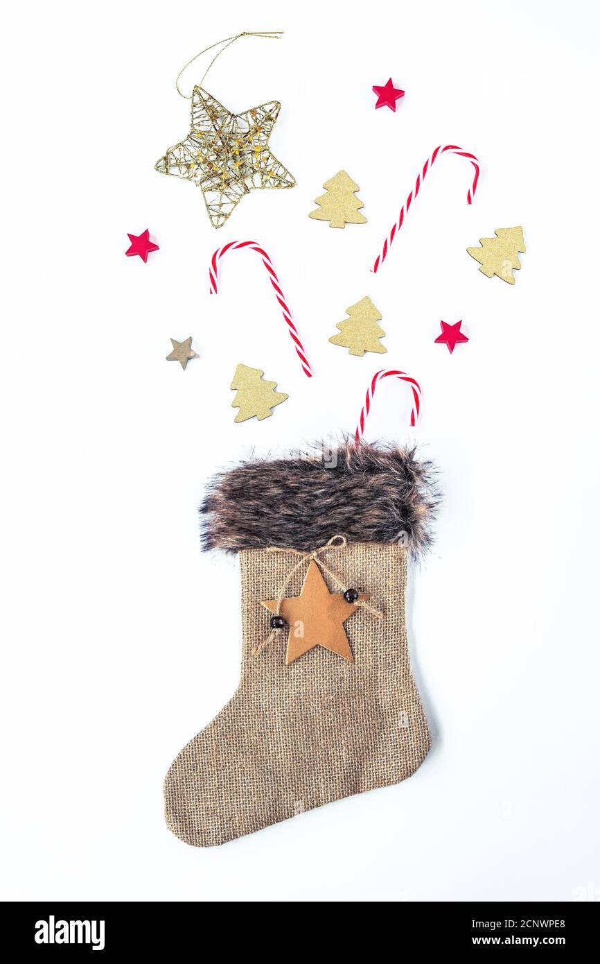 Giocattoli di Natale e canna caramella in calza di natale fatta di sackcloth su sfondo bianco. Disposizione piatta, vista dall'alto. Foto Stock