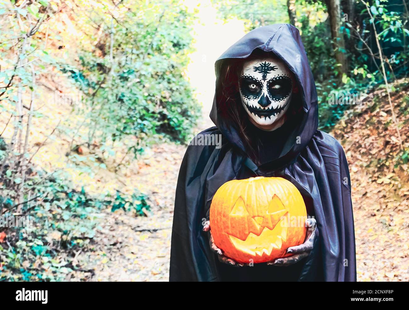 Giovane donna con maschera di vernice halloween con cappuccio nero - la  strega spaventosa che tiene lo spookey ha affamato la zucca Foto stock -  Alamy