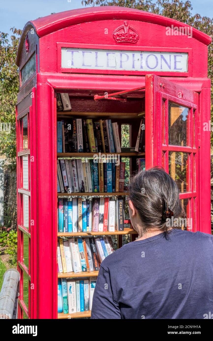 Donna che guarda una scatola telefonica nel villaggio Norfolk di West Newton, ora utilizzato come una biblioteca di rilliage. Foto Stock
