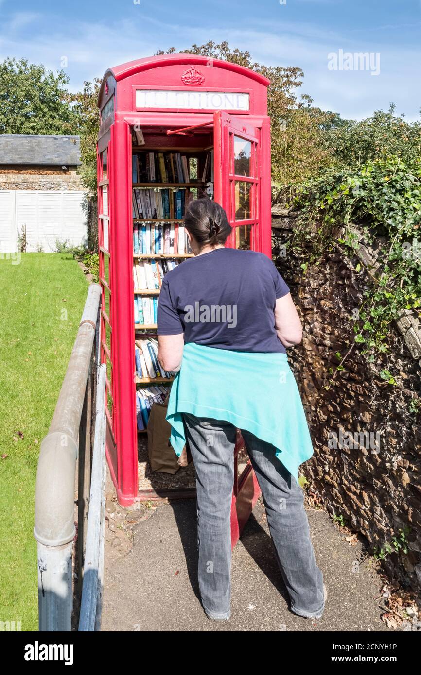 Donna che guarda una scatola telefonica nel villaggio Norfolk di West Newton, ora utilizzato come una biblioteca di rilliage. Foto Stock
