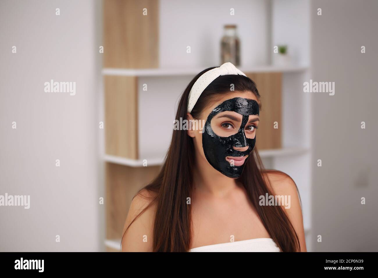 Giovane donna con maschera nera detox di carbonio sul viso, la ragazza adolescente si prende cura della pelle oleosa, pulizia dei pori. Salone di bellezza. Cura della pelle. Foto Stock