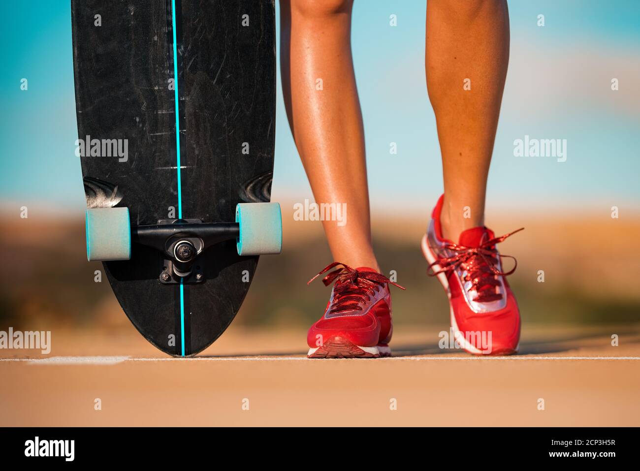 Indossate la donna con le gambe abbronzate in eleganti sneaker rosse contiene skateboard Foto Stock