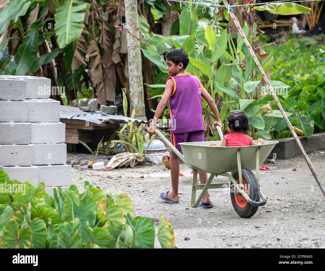 FUAHMULAH ISLAND, MALDIVE - 11 APRILE 2017: Un ragazzo rotola la sorella in una carriola mentre i loro genitori costruiscono una casa Foto Stock