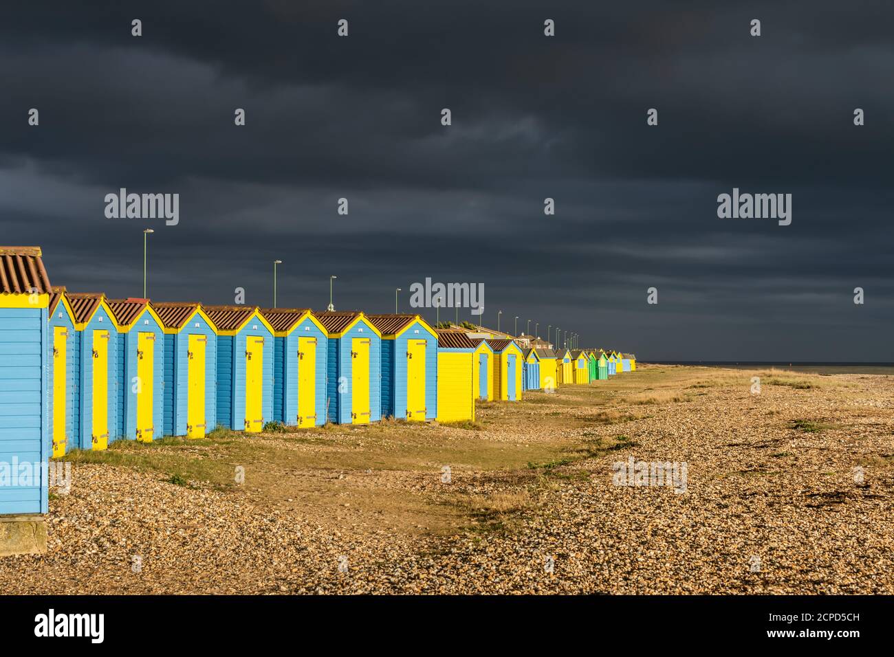 Dark nuvole temporalesche avvicinando il lungomare nella luce del giorno con il sole illuminazione cabine sulla spiaggia, in Littlehampton, West Sussex, in Inghilterra, Regno Unito. Foto Stock