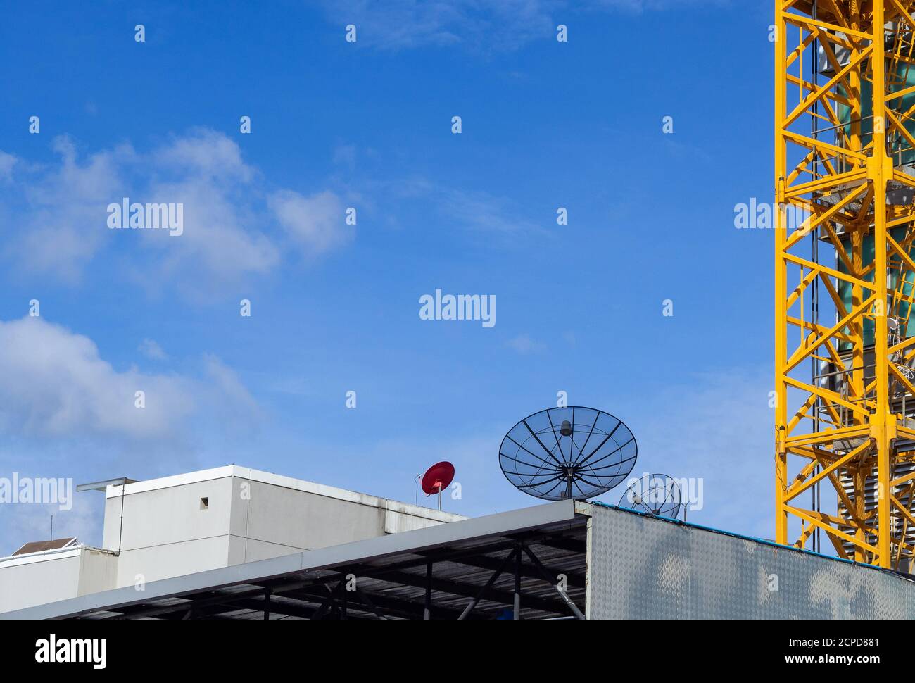 Cantiere con gru sullo sfondo del cielo e satelliti sull'edificio. Grande attrezzo giallo di costruzione di macchine gru dell'industria edile Foto Stock