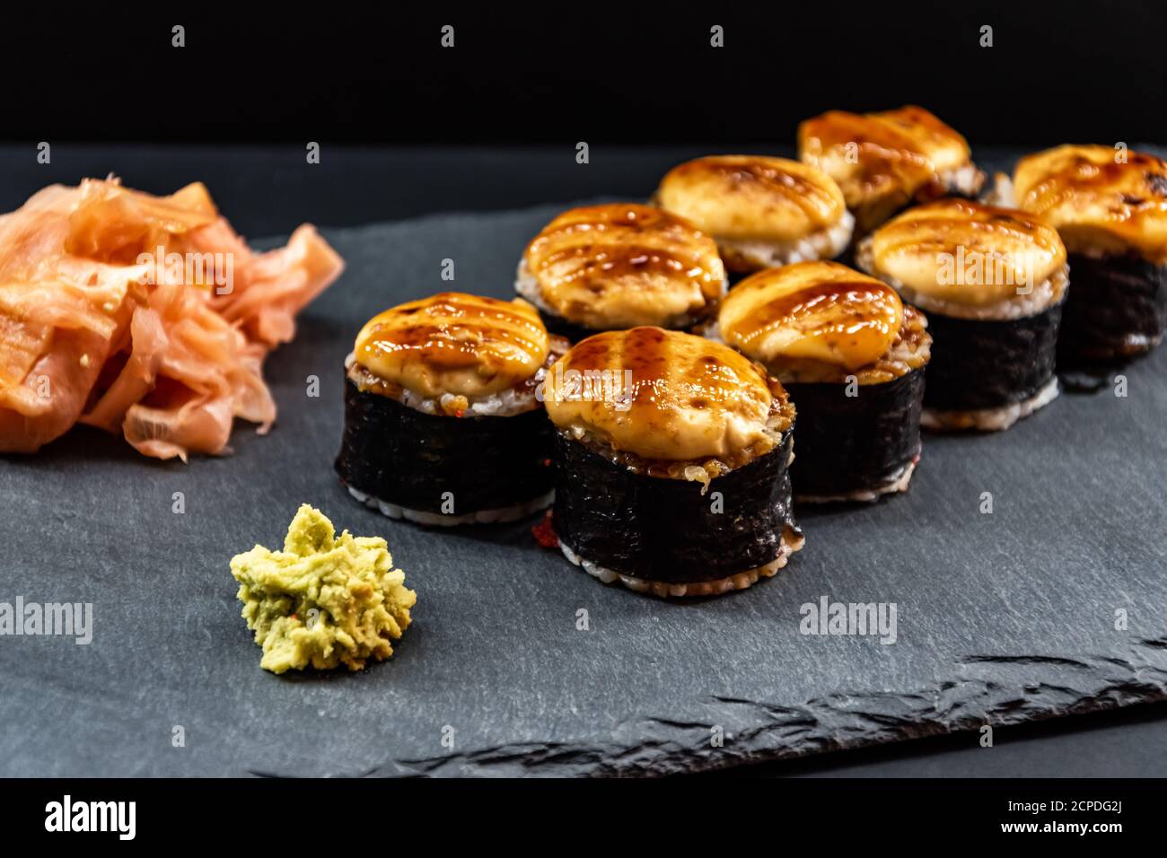 Servito sushi caldo arrotolato in fogli di nori con zenzero e wasabi su un piatto di pietra nera. Foto Stock