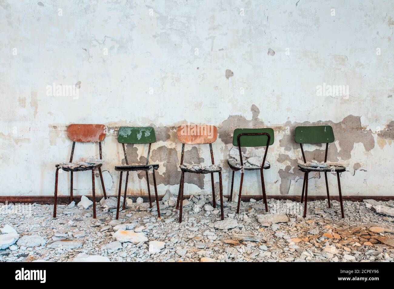 cinque piccole sedie fianco a fianco in un vecchio edificio abbandonato, macerie e polvere, peeling muro Foto Stock